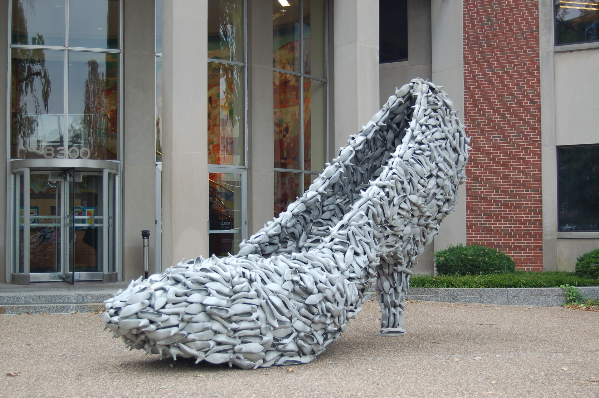 photograph of a stiletto heel shoe that is made of many heeled shoes. The sculpture is located in front of a building