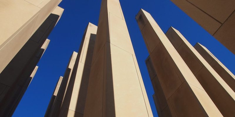 A concrete cluster of obelisks extend towards a bright blue sky.