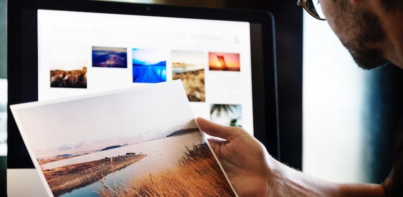 A man holds an image of a river in front of a computer monitor.