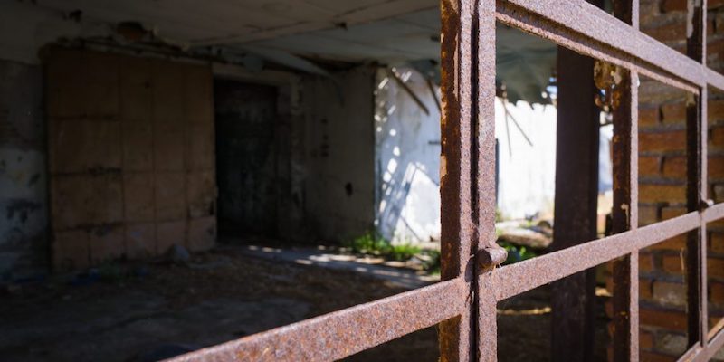 A view of an empty, abandoned room through a rusted, paneless window.