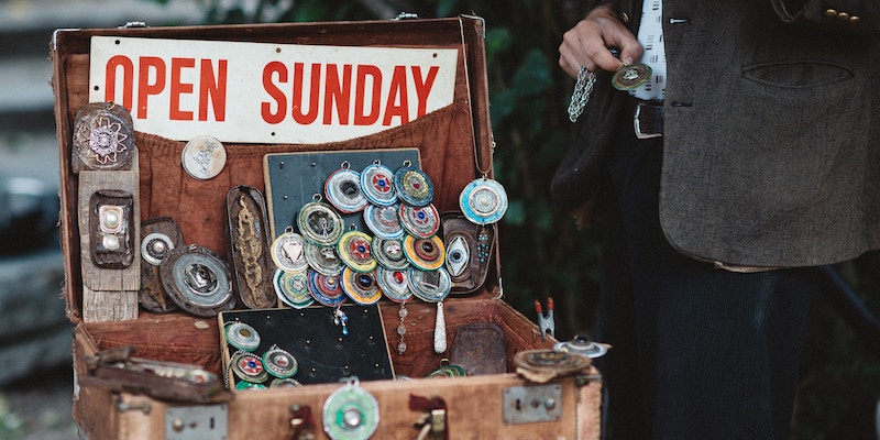 A street vendor stands near a suitcase with knick-knacks for sale.