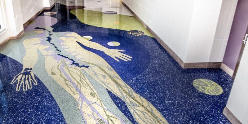 A depiction of the human body made of yellow, purple, blue, and green epoxy terrazzo is accented with metal on the Health Sciences Center building floor at Texas Tech University.