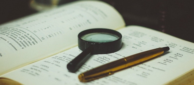 A magnifying glass and pen sit atop an open book.