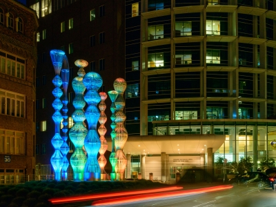 8 stainless steel sculptures with colored lights to the left of a building