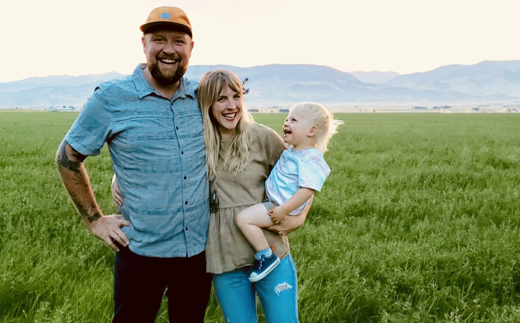 Picture of a family in front of green. Eliza, her husband and child