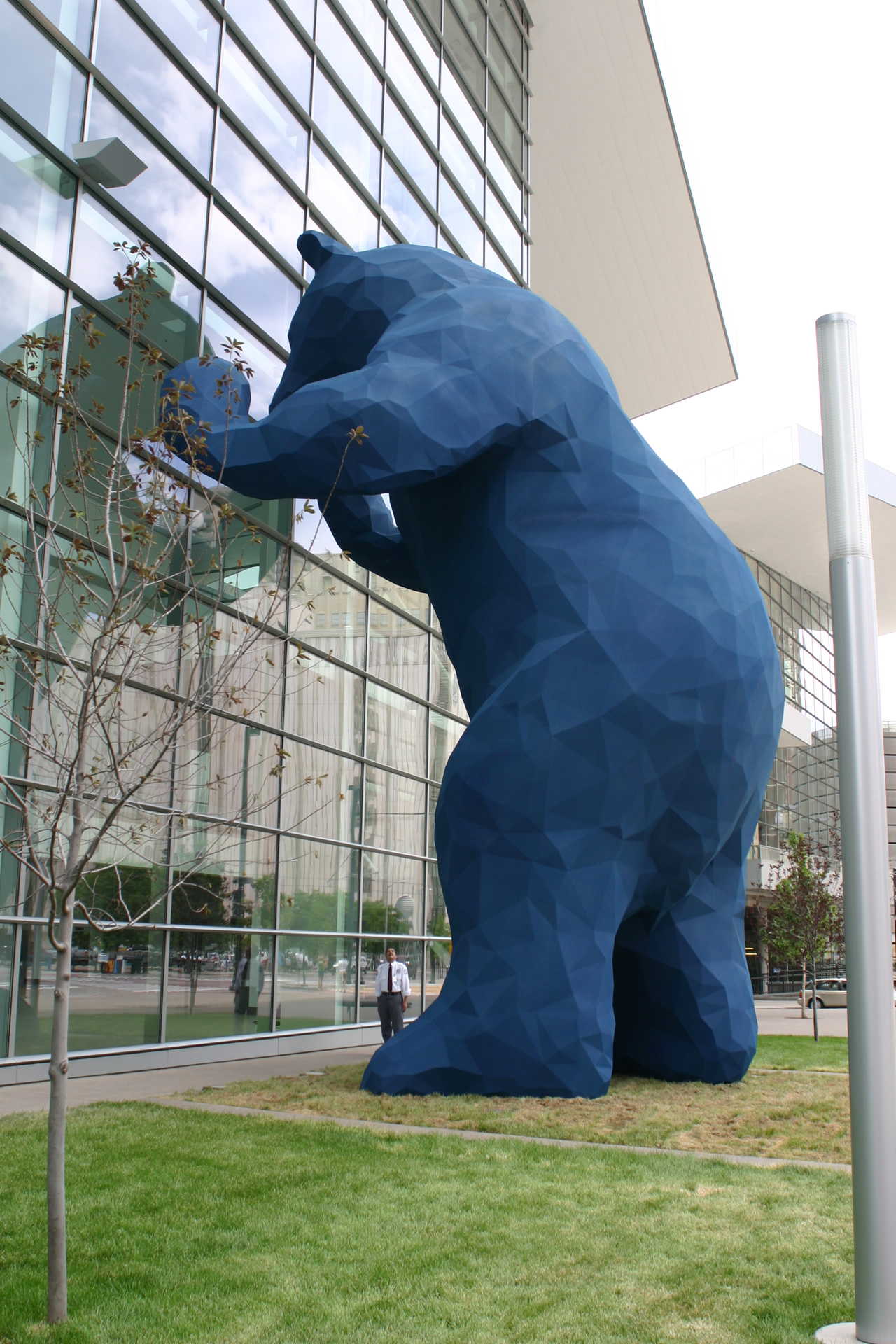 photograph of a sculpture that is a big blue bear that appears to be peering into a glass building
