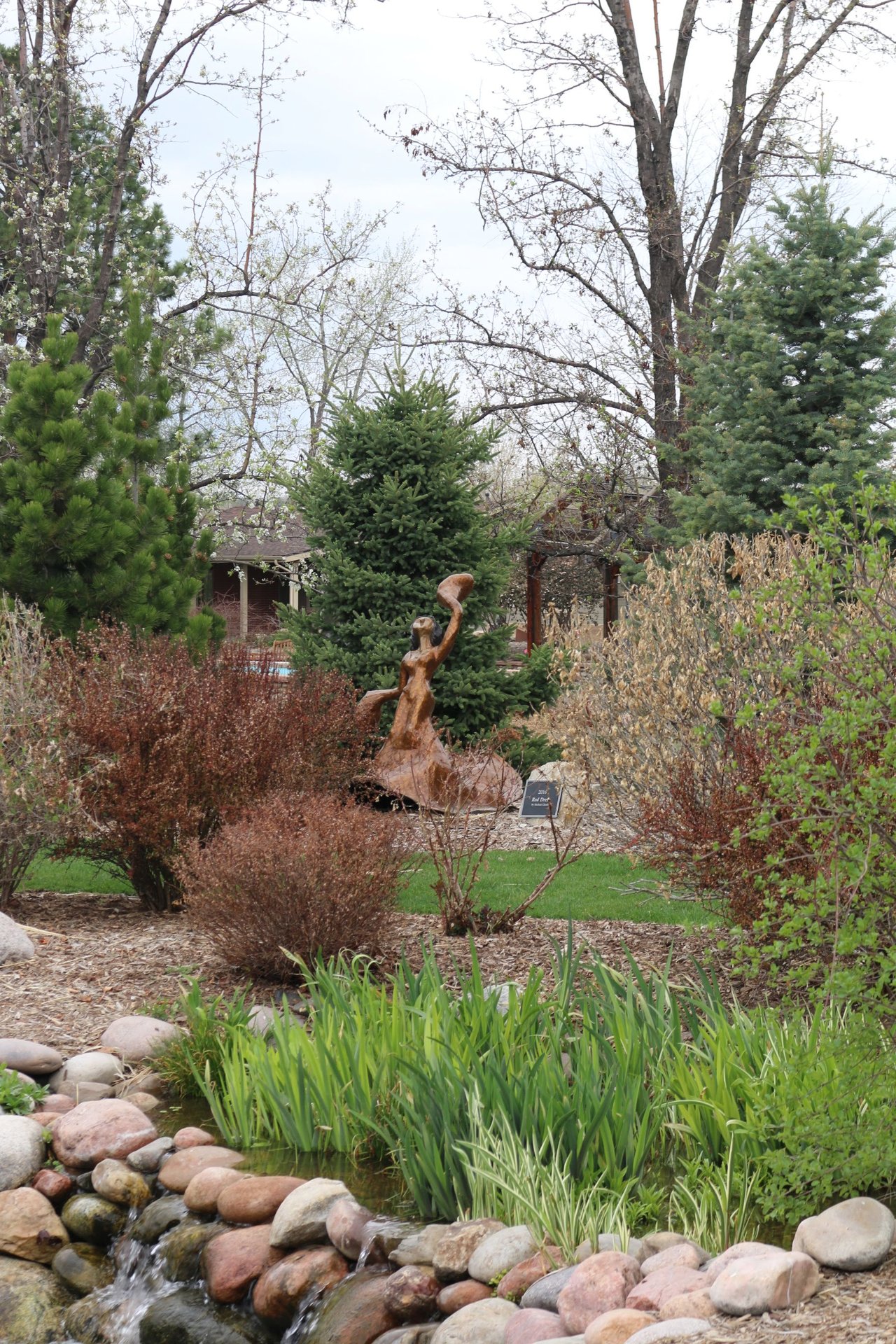 photograph of a copper sculpture of a dancing girl nested in greenery and rock landscape