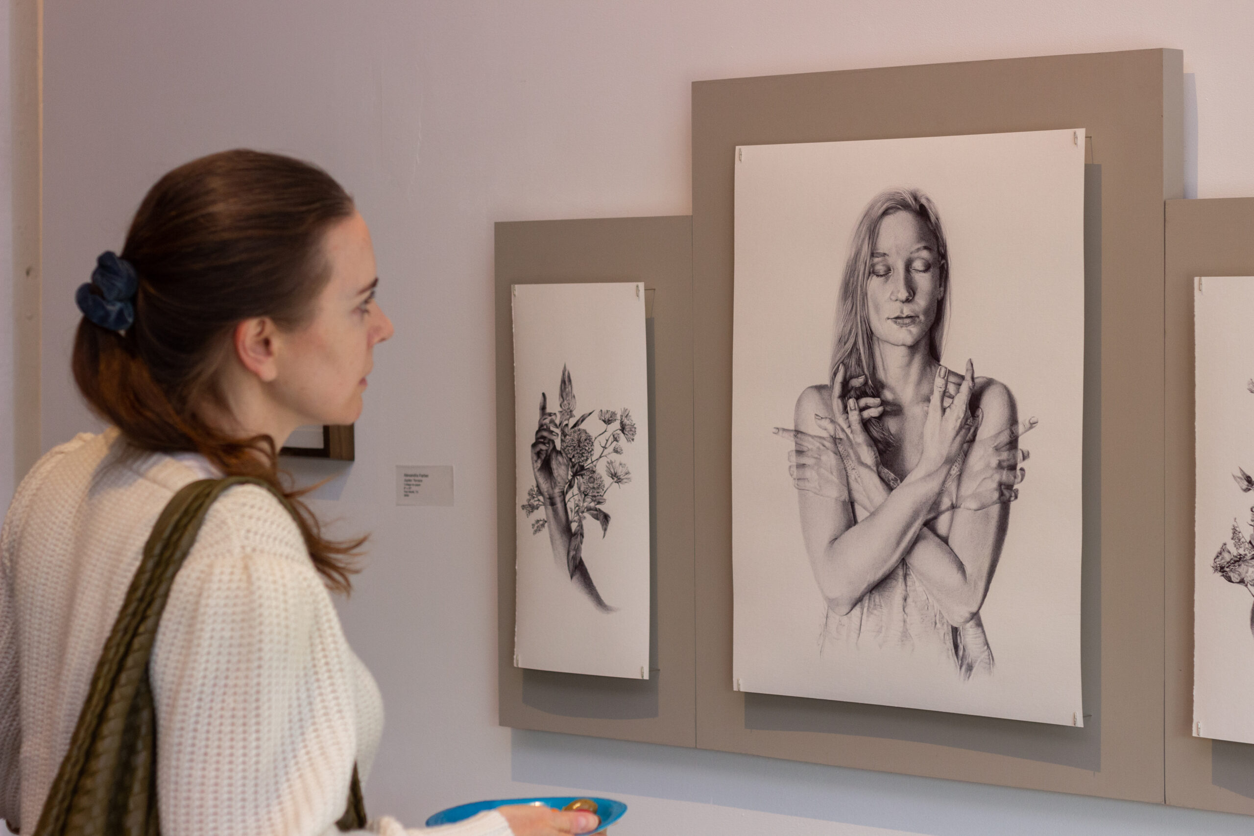 close up photo of a woman looking at a pice of drawn artwork hung on a white wall
