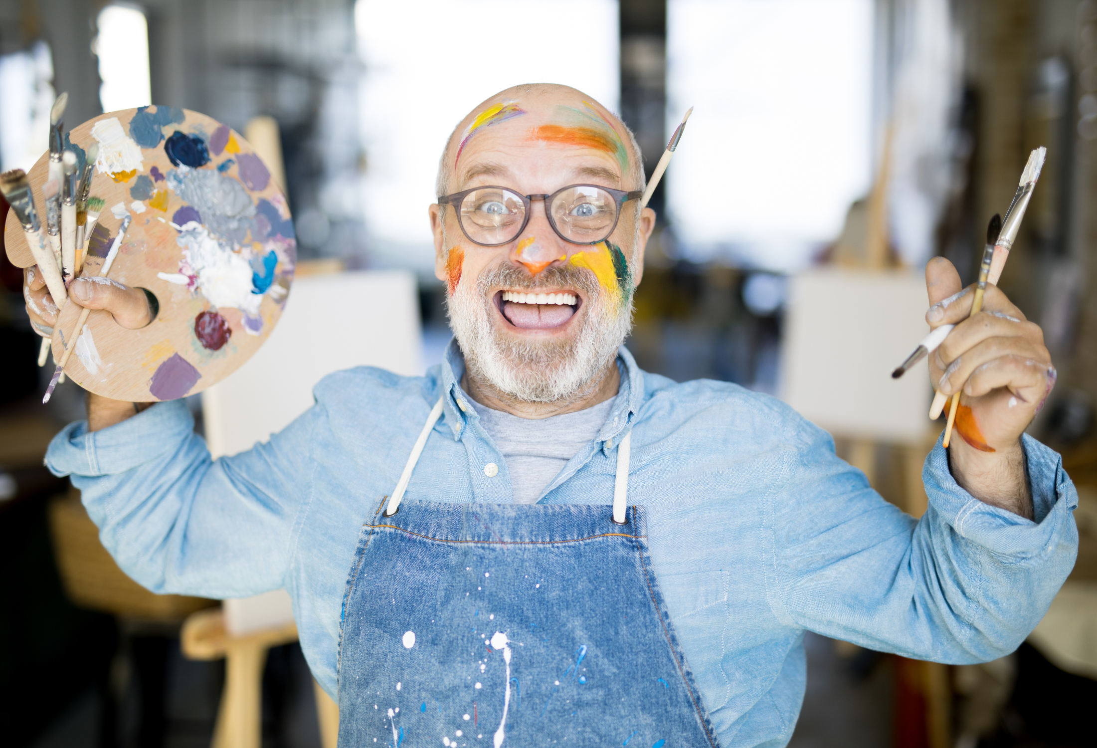 Image of a man holding paintbrushes and a palette and smiling