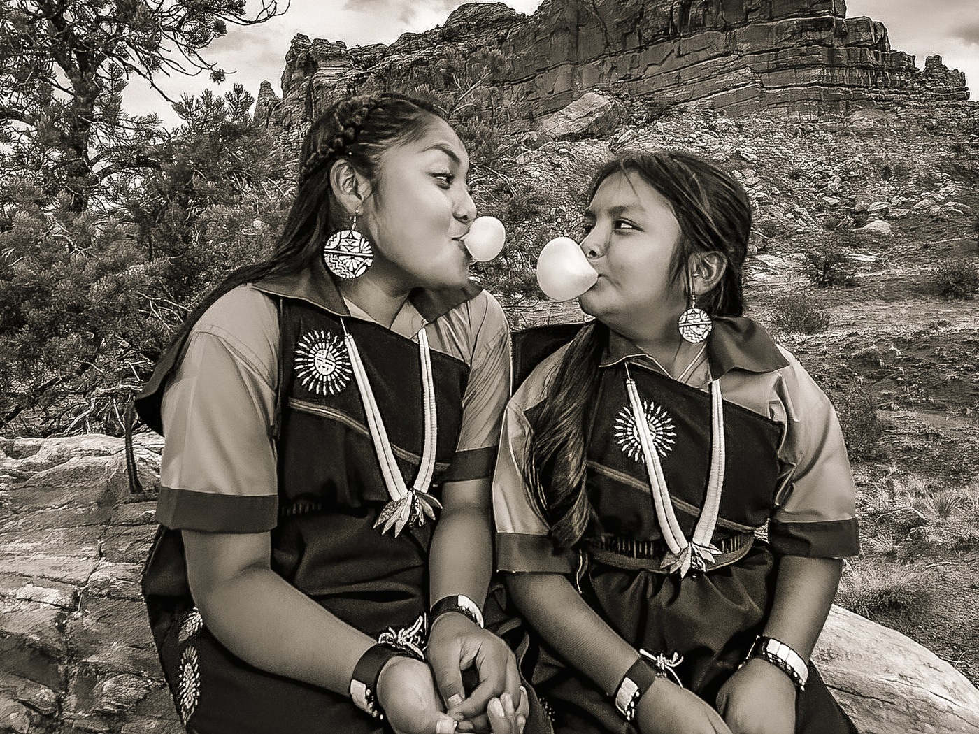 Two young women dressed in traditional native clothing and blowing bubble gum bubbles.