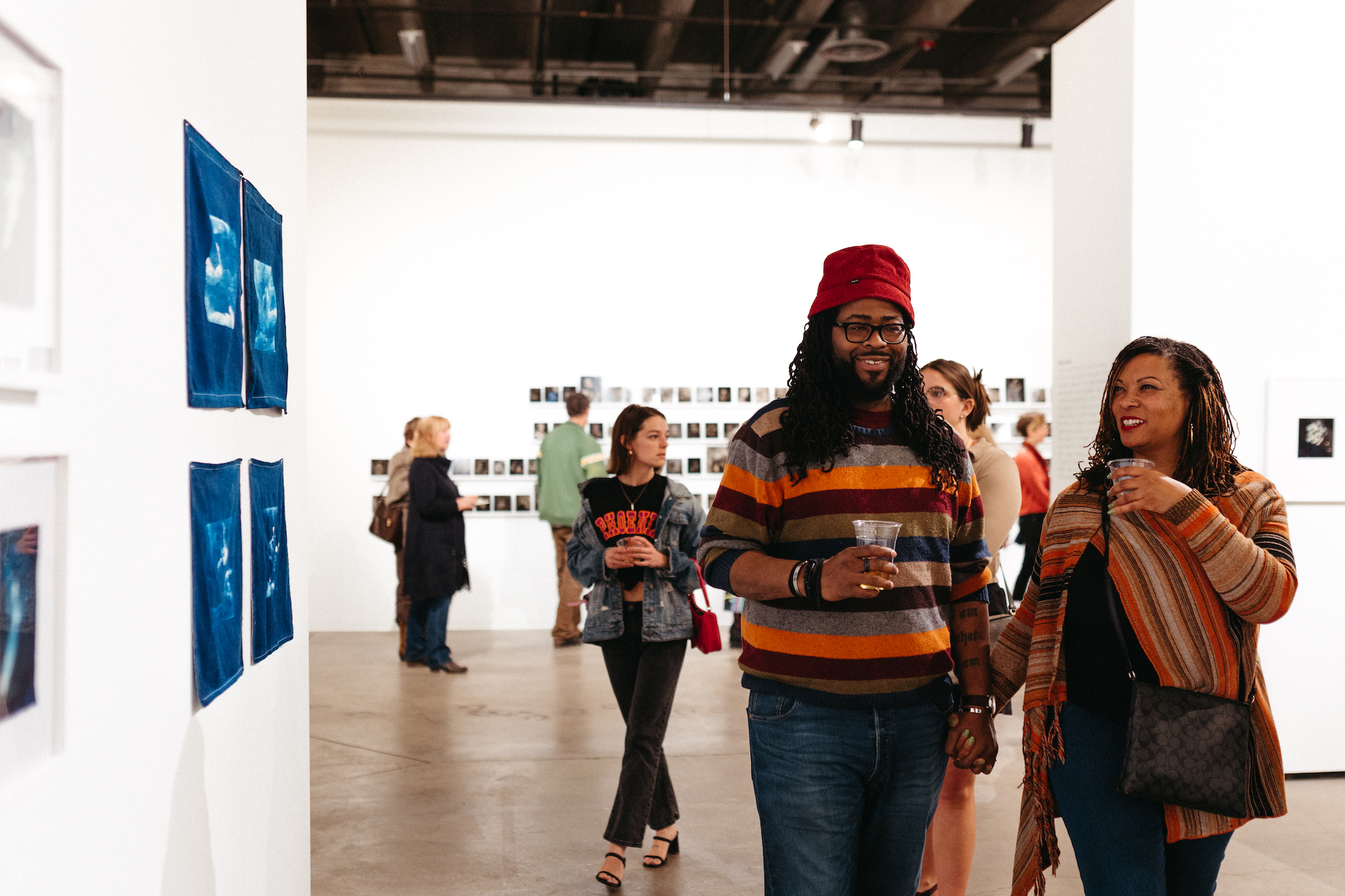 Two people smiling while standing next to art handing on a wall