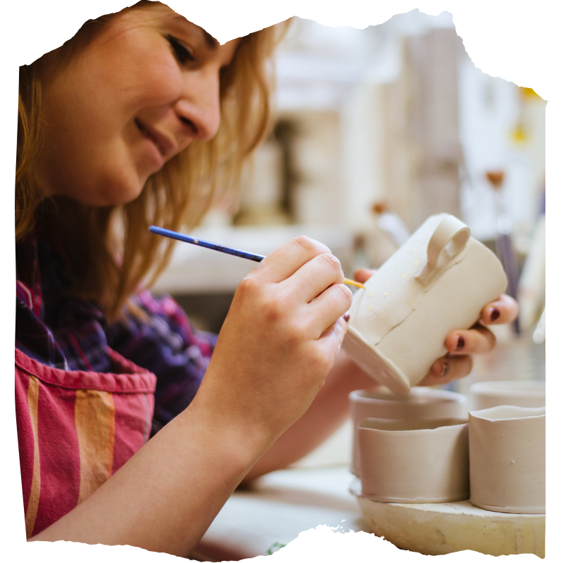 Female artist working with ceramics, painting a clay mug.